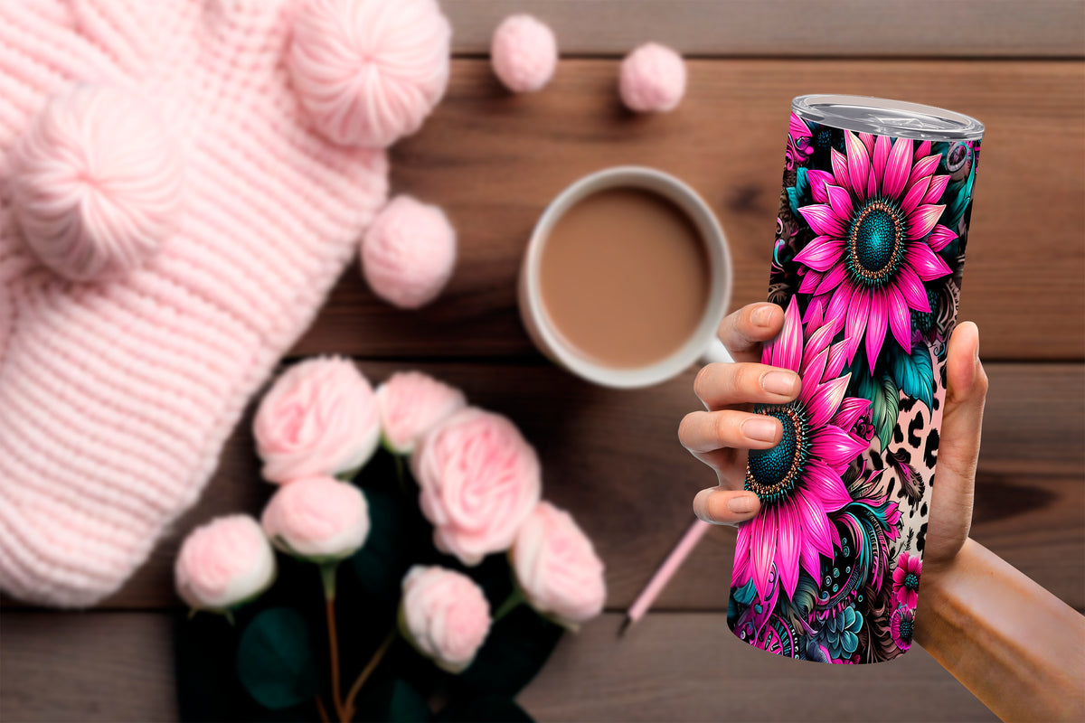 20oz pink tumbler with vibrant floral and leopard print design held over wooden table with coffee and pink knitwear