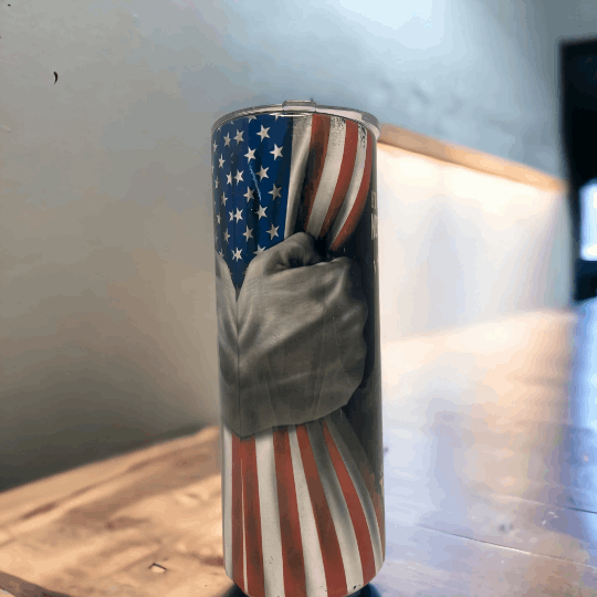 20oz tumbler with american flag design and a grayscale hand gripping the flag on a wooden surface